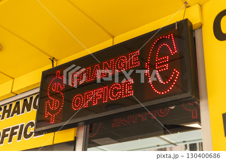 A vibrant neon illuminated sign indicates a currency exchange office, with dollar and euro symbols prominently displayed. The busy city atmosphere surrounds the area A vibrant neon illuminated sign indicates a currency exchange office, with dollar and euro symbols prominently displayed. The busy city atmosphere surrounds the area 130400686