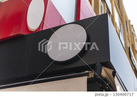 A blank black circular sign mounted on a building facade is devoid of any logo or text. The surrounding architecture features colorful elements, reflecting a vibrant urban environment 130400717