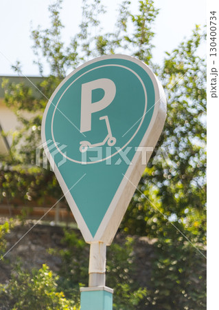 Brightly colored parking sign indicates designated area for electric scooters among lush greenery, providing a convenient option for urban transport during the day 130400734