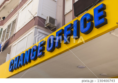 A vibrant yellow sign reading CHANGE OFFICE catches attention in an urban location 130400743