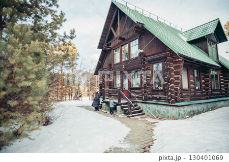 wooden log house with green roof in snowy winter forest with people near entrance, rustic cabin architecture and concept of countryside vacation in cold season wooden log house with green roof in snowy winter forest with people near entrance, rustic cabin architecture and concept of countryside vacation in cold season 130401069