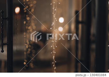close up of glowing string lights with warm bokeh effect in festive interior with blurred silhouette, concept of cozy home atmosphere and Christmas holiday decoration 130401084