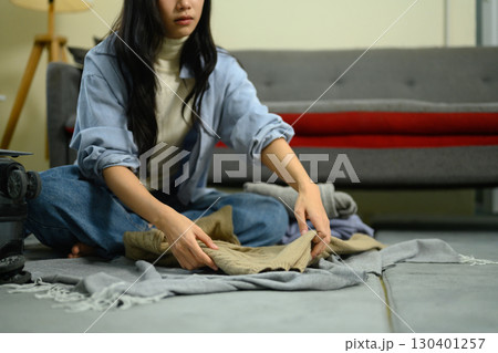 Female traveler organizing outfits on the floor next to suitcase before trip 130401257