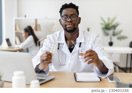 Male doctor of African descent holding medicine and water in professional office setting Male doctor of African descent holding medicine and water in professional office setting 130401288