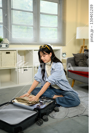 Traveler getting ready for vacation, organizing clothes inside suitcase on floor 130401289