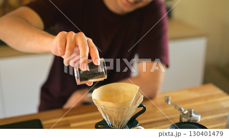 Close up of a man pouring freshly ground coffee into a paper filter for pour over brewing Close up of a man pouring freshly ground coffee into a paper filter for pour over brewing 130401479