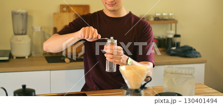 Man grinding fresh coffee beans with a manual coffee grinder in a cozy home kitchen 130401494