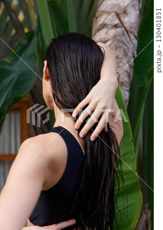 Tropical paradise Woman with long black hair standing near palm tree with hands on head 130401851