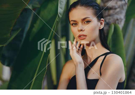 Gorgeous young woman posing gracefully in front of lush palm trees with hand on chin under the sun 130401864