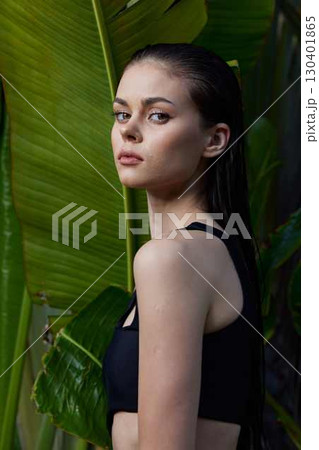 Attractive young woman standing in front of a palm tree in a black sports bra top 130401865