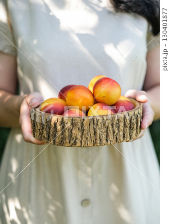 Woman in beige dress holds rustic wooden bowl filled with vibrant ripe nectarines, symbolizing summer harvest and fresh organic food. Ideal for food blogs, social media and healthy lifestyle content Woman in beige dress holds rustic wooden bowl filled with vibrant ripe nectarines, symbolizing summer harvest and fresh organic food. Ideal for food blogs, social media and healthy lifestyle content 130401877