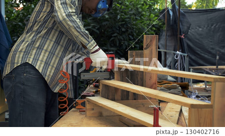 Worker in safety gear using nail gun to secure wooden planks on staircase frame construction 130402716