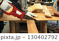 Worker cutting wooden plank with red electric saw on workbench wearing white gloves and striped shirt 130402792