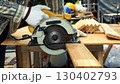 Worker cutting wooden plank with yellow circular saw on workbench while wearing white gloves and striped shirt 130402793