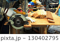 Carpenter cutting wooden plank with circular saw on workbench while wearing gloves and protective mask 130402795