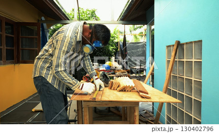 Carpenter measuring wooden plank on workbench with ruler while wearing safety mask and gloves Carpenter measuring wooden plank on workbench with ruler while wearing safety mask and gloves 130402796