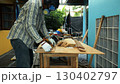 Carpenter measuring wooden plank with tape measure on workbench while wearing safety mask and gloves 130402797