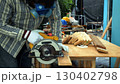 Carpenter cutting wooden plank with circular saw on workbench while wearing safety mask gloves and protective gear 130402798