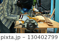 Carpenter cutting wooden board with circular saw on workbench while wearing safety mask gloves and protective gear 130402799