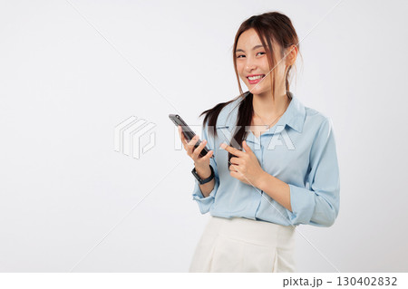 Asian woman smiling holds phone and points with excitement, capturing a fun, connected moment that expresses happy lifestyle and joy of using modern mobile technology. isolated studio white background 130402832