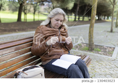 Senior woman reading a book on park bench, taking off her glasses 130403023
