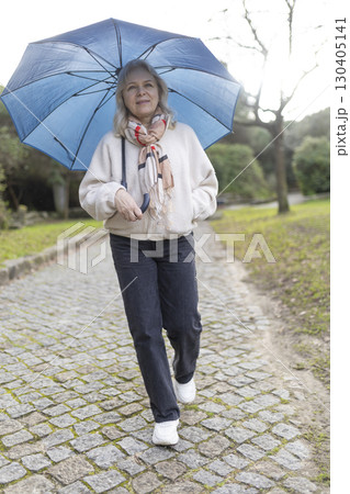 Senior woman walking in park with umbrella on cloudy day Senior woman walking in park with umbrella on cloudy day 130405141