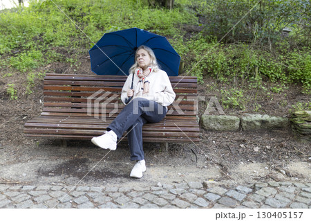 Senior woman holding umbrella sitting on bench in park after rain Senior woman holding umbrella sitting on bench in park after rain 130405157