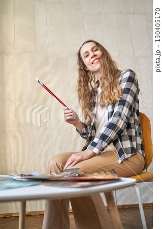 Young caucasian female artist smiling while holding paintbrush in studio Young caucasian female artist smiling while holding paintbrush in studio 130405170