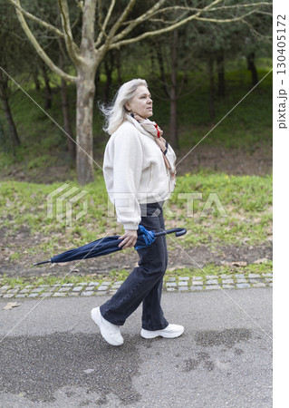 Senior woman walking in park holding closed umbrella after rain Senior woman walking in park holding closed umbrella after rain 130405172