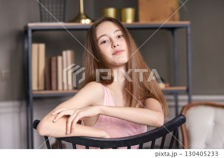 Young caucasian female sitting on chair in modern room with books and decor 130405233