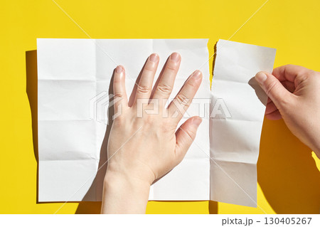 Caucasian female hands tearing white paper on bright yellow background Caucasian female hands tearing white paper on bright yellow background 130405267