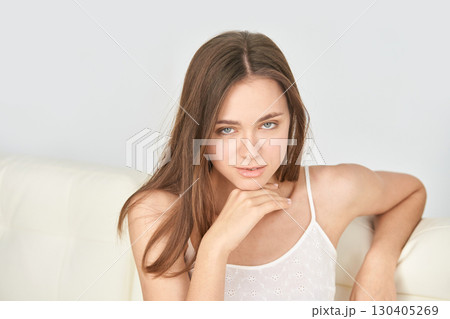 Young caucasian female with long brown hair relaxing on sofa in casual white Young caucasian female with long brown hair relaxing on sofa in casual white 130405269