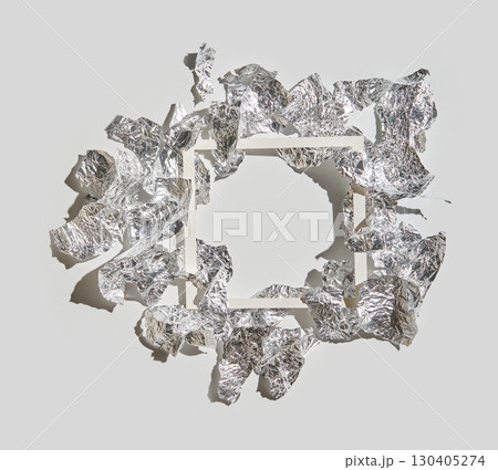 Abstract art with crumpled silver foil surrounding empty white frame on gray 130405274