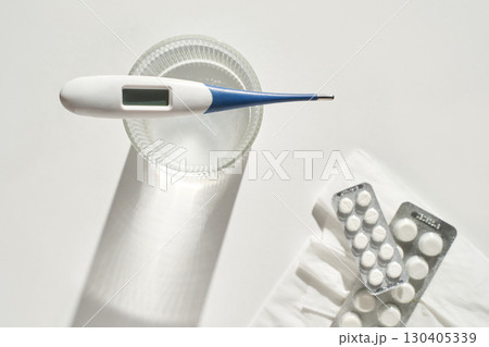 Digital thermometer and pills on white background with glass of water Digital thermometer and pills on white background with glass of water 130405339
