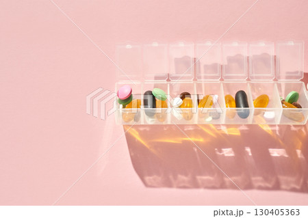 Assorted pills in weekly organizer on pink background with shadows 130405363