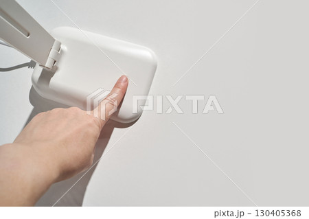 Female hand touching minimalist white desk lamp on clean surface with wired 130405368