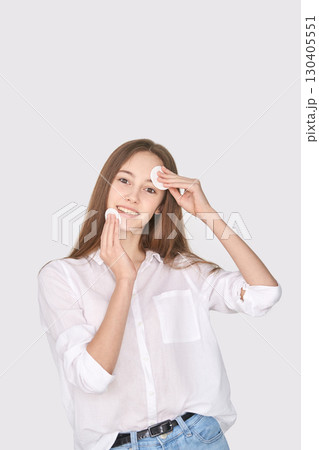 Young caucasian female teen using cotton pads for skincare routine in white 130405551