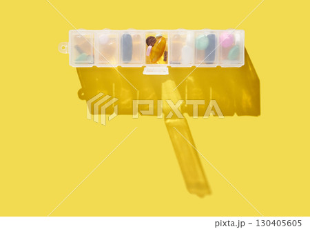 Organized weekly pill box with various medicines on bright yellow background 130405605