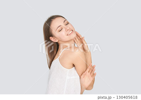Smiling young caucasian female posing happily in white top against grey 130405618