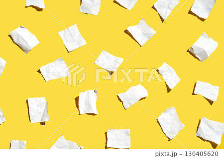 Scattered white torn paper on vibrant yellow background creating abstract art 130405620