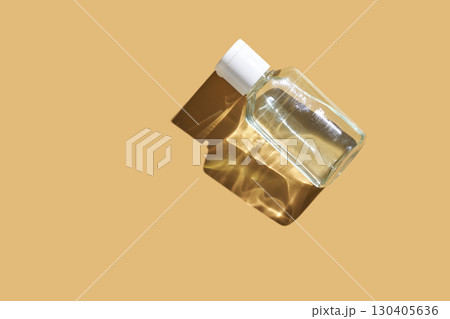 Transparent glass perfume bottle with white cap casting shadow on beige Transparent glass perfume bottle with white cap casting shadow on beige 130405636