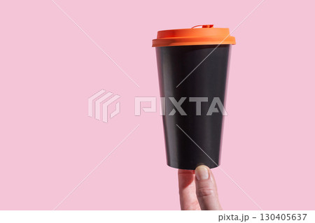 Reusable black coffee cup with orange lid held by hand against pink background Reusable black coffee cup with orange lid held by hand against pink background 130405637