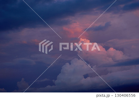 暗い空を背景に夕日に染まる入道雲。夏らしい雲と空の背景用素材。 暗い空を背景に夕日に染まる入道雲。夏らしい雲と空の背景用素材。 130406556