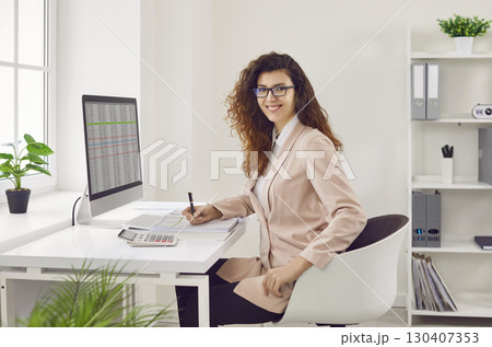 Happy smiling business woman accountant working on PC computer with tables on her workplace. 130407353