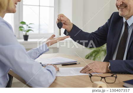 Smiling man real estate agent hands over the key to a happy young woman house owner Smiling man real estate agent hands over the key to a happy young woman house owner 130407357