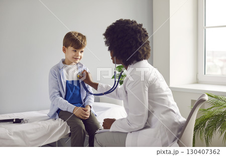 Doctor with stethoscope examining child's lungs and heart rate sitting on the couch in office. 130407362