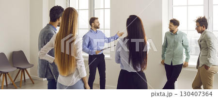 Business coach or team manager with a clipboard talking to a group of people in the office 130407364