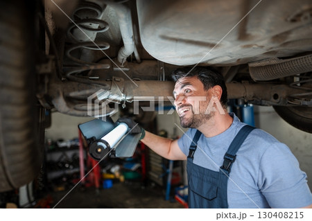 Mechanic inspecting car's undercarriage with a flashlight in a garage 130408215