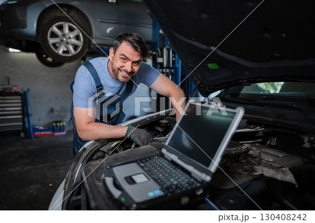 Car mechanic using a computer to diagnose a car engine problem 130408242
