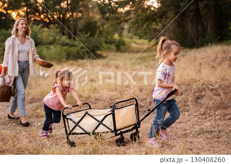 Mother and daughters pulling a cart, enjoying a picnic in the woods Mother and daughters pulling a cart, enjoying a picnic in the woods 130408260